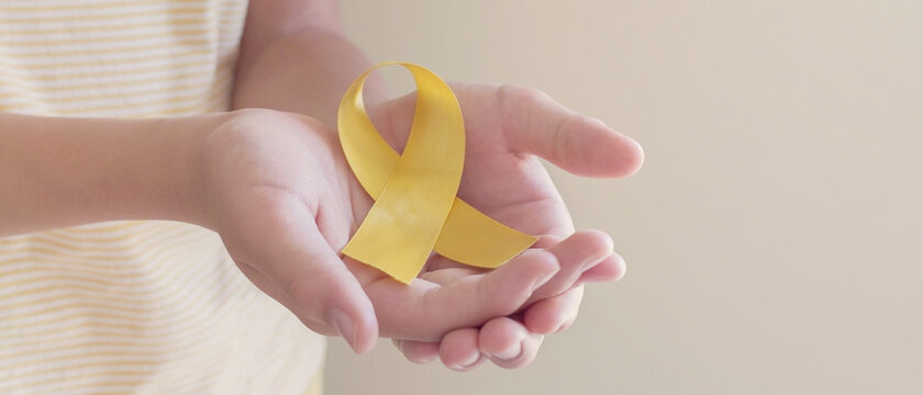 Hands holding yellow gold ribbon, Sarcoma Awareness, Bone cancer, childhood cancer awareness, September yellow, World Suicide Prevention Day concept