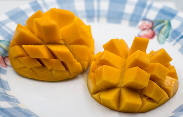 Sliced ripe mangoes up close looking bright orange on a fruit themed blue bordered plate
