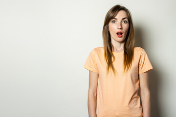 Obraz premium Young friendly girl with a surprised face in a t-shirt on a light background