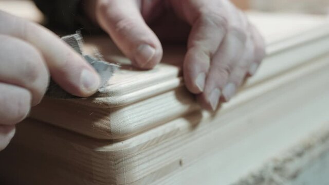 Close-up of a man's hands sanding beveled edges as he puts the final touches on a woodworking project.