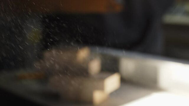 Sawdust particles fly in the air while a defocused carpenter works in the background.