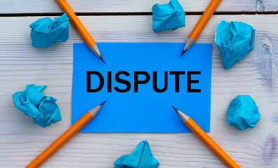 DISPUTE - word on blue paper on a light background with crumpled pieces of paper and pencils