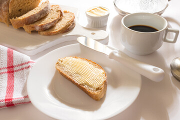 Mesa com Café da Manha: Pão Integral com manteiga, chícara de café, bule com café, toalha vermelha xadrez, pão integral fatiado sobre tábua branca, manteiga no ramequim, pão com manteiga Ponto de vist