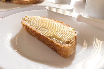 Mesa com Café da Manha: Pão Integral com manteiga, chícara de café, bule com café, toalha vermelha xadrez, pão integral fatiado sobre tábua branca, manteiga no ramequim, pão com manteiga Ponto de vist