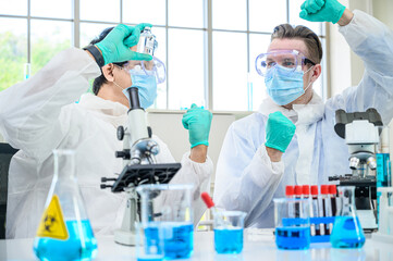 Couple male scientist wearing protection suit holding Coronavirus vaccine and working with many lab equipment for research vaccine at laboratory.