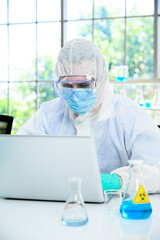 Male scientist wearing protection suit working with computer laptop and many lab equipment for research at laboratory.