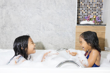 A couple of Asian childhood siblings happily played in the bathtub bubble.