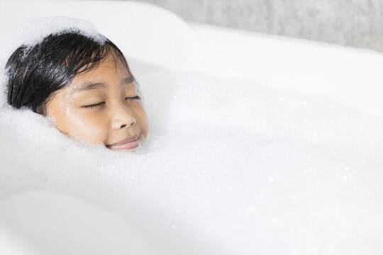 An Asian girl is happily soaking in a bubble bath.