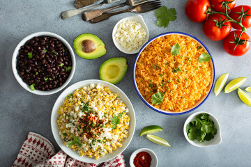 Mexican food on the table, variety of side dishes, street corn, mexican rice and baked beans