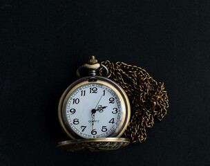 Dhaka, Bangladesh - April 25, 2020: A fashionable pocket watch with a golden chain in black background. Happy home photography during the quarantine. Stay home, stay safe.