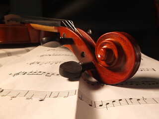 Closeup of the pegs and scroll of a violin on sheet music