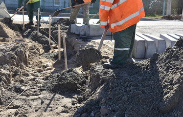 Workers shovel cement into a hole, installing a road curb, repairing the road.