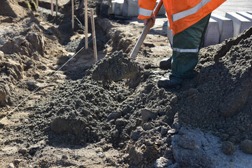 A worker in overalls throws cement into a pit, construction of a highway.