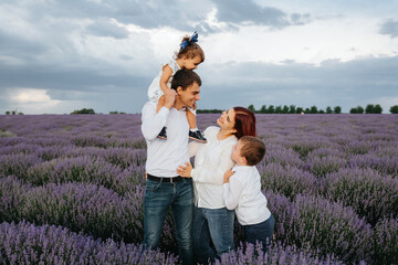 Young happy family: father, mother, son and daughter are in the middle of the lavender field and looking at each other