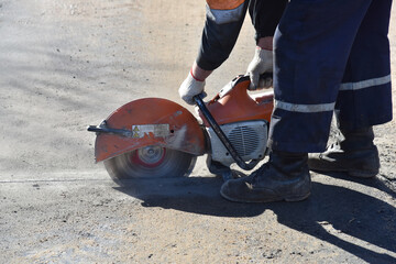 Obraz premium The builder uses a circular saw to cut part of the asphalt surface.