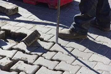 A worker lifts a road tile with an iron bar.