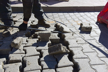 The builder raises the concrete slab with an iron rod, repairs the road surface.