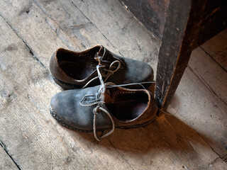 Pair of old worn out leather retro shoes on a vintage wooden floor by the table.  Historical...