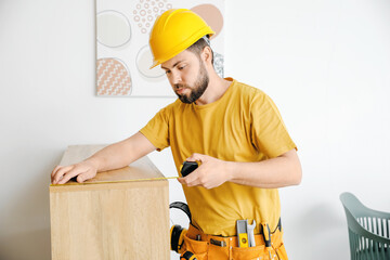 Male carpenter using tape measure in room