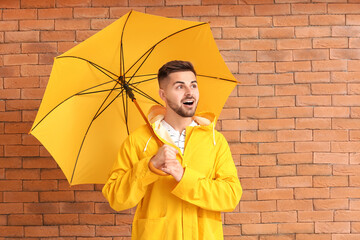Young man in raincoat and with umbrella on brick background