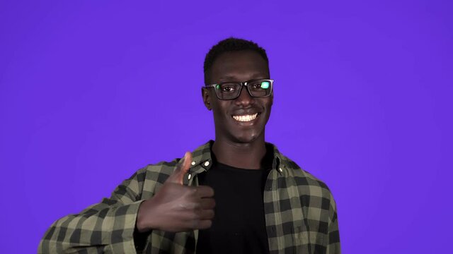 Happy, smiling african american man in good mood on blue background. Man in stylish glesses gesturing with thumbs up, like gesture and tooty smiling - human emotions