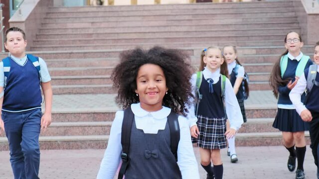 little African-American girl with friends in school uniform goes down stone stairs by school building on warm day slow motion