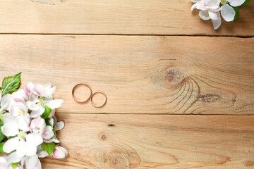 Two gold rings on a wooden background with white Apple blossoms. Wedding in eco-style, rustic. Couple in love, ceremony and registration, details, bride's fees, groom's morning. Space for text. flatly