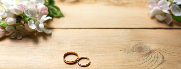 Two gold rings on a wooden background with white Apple blossoms. Wedding in eco-style, rustic. Couple in love, ceremony and registration, details, bride's fees, groom's morning. Space for text. flatly