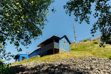 A blue railway box against a blue sky. The house is visible through the branches of trees. High quality photo