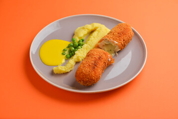 Cordon bleu cutlet, deep fried meat served with mashed potatoes and green peas on gray plate over orange background.