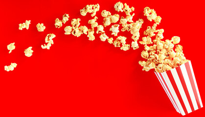 popcorn in the classic red and white bucket splashing  out of the box with shadow in red background