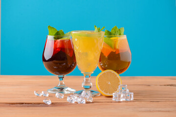 Three tropical mixed drinks with lime and lemon and mint leaves served in different glasses on rustic wooden table.