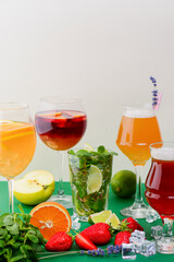 Five tropical mixed drinks, orange, lemon and raspberries cocktails over bright pastel green background.