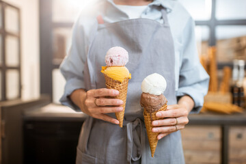 Female seller holding two yummy ice creams in waffle cone at the shop, close-up