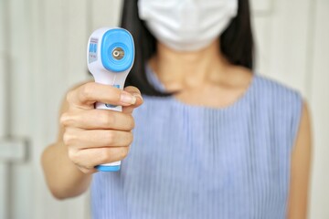 Staff wearing protecting face mask use non contact digital thermal scanner temperature gun at entrance. Concept of protection Covid flu. Control people to enter shopping mall, supermarket, canteen.