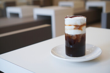 Einspanner coffee. A cup of americano coffee topped with fresh cream, whipped cream and cocoa powder on white plate at cafe. (Copy space, isolated)