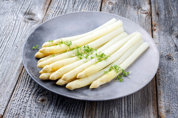 Traditioneller gedünsteter weißer Spargel mit Kräuter als close-up auf einem Modern Design Teller auf einem Holz Tisch mit Textfreiraum