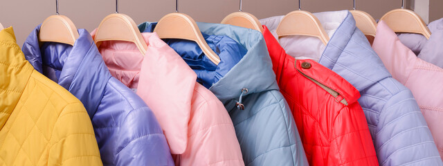 New collection of down jackets on hangers in the market. Colorful background of modern spring, autumn outerwear.
