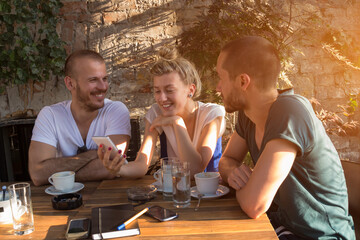 Friends enjoying morning / evening coffee in a coffee-shop and using modern smartphone.