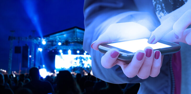 Woman Using Modern Smartphone At Night With Blurred Concert Lights In Background.