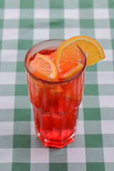 One tropical mixed drink, berries and orange cocktail served on green plaid tablecloth.