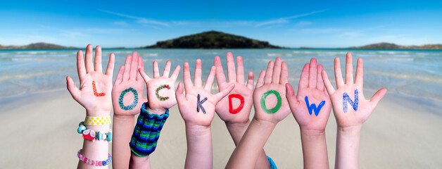 Kids Hands Holding Colorful English Word Lockdown. Ocean And Beach As Background