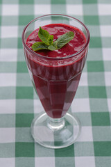 One tropical mixed drink, berries and mint cocktail served on green plaid tablecloth.