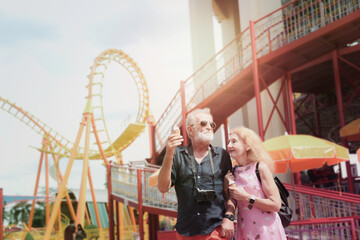 Elderly couple spending time together at theme park on summer weekend, senior people hanging out and having fun at an amusement park.