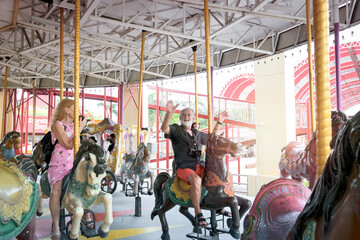 Fototapeta na wymiar Elderly couple spending time together at theme park on weekend, senior people hanging out and having fun at amusement park. Grandpa and grandma enjoying at carousel spinning