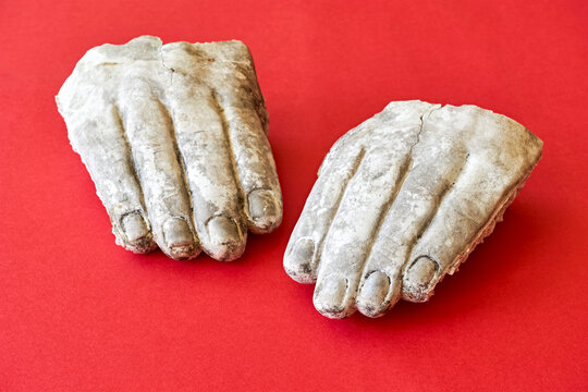 Two White Weathered Broken Hands Of A Stone Statue On A Red Background. Iconoclasm Concept.