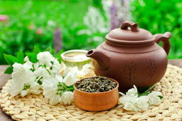 Chinese tea cerermony in the garden. Clay teapot with glass cup, dry green tea and jasmine flower on a wicker napkin.