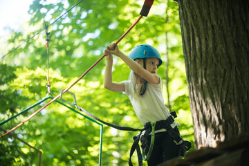Rope adventure - a little girl standing on high by the tree and holding by the ropes with her hands