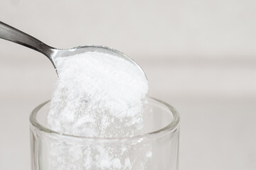 White tasteless creatine powder on a teaspoon spills out into a transparent glass. Sports...