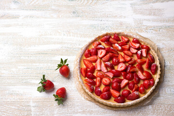 Summer tart with custard of baked milk and juicy fresh strawberries on light wooden background, top view, horizontal	